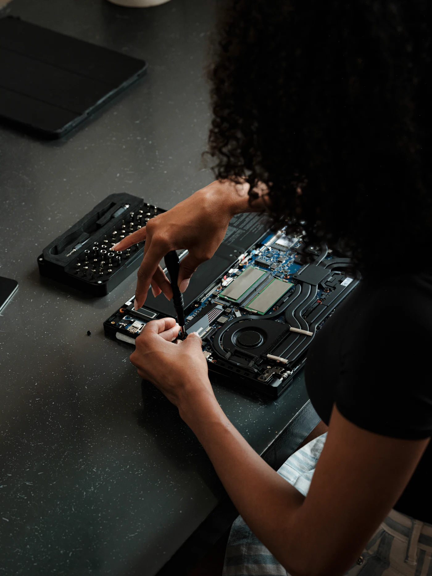 Iemand opent aan tafel een laptop met een schroevendraaier om hem te upgraden