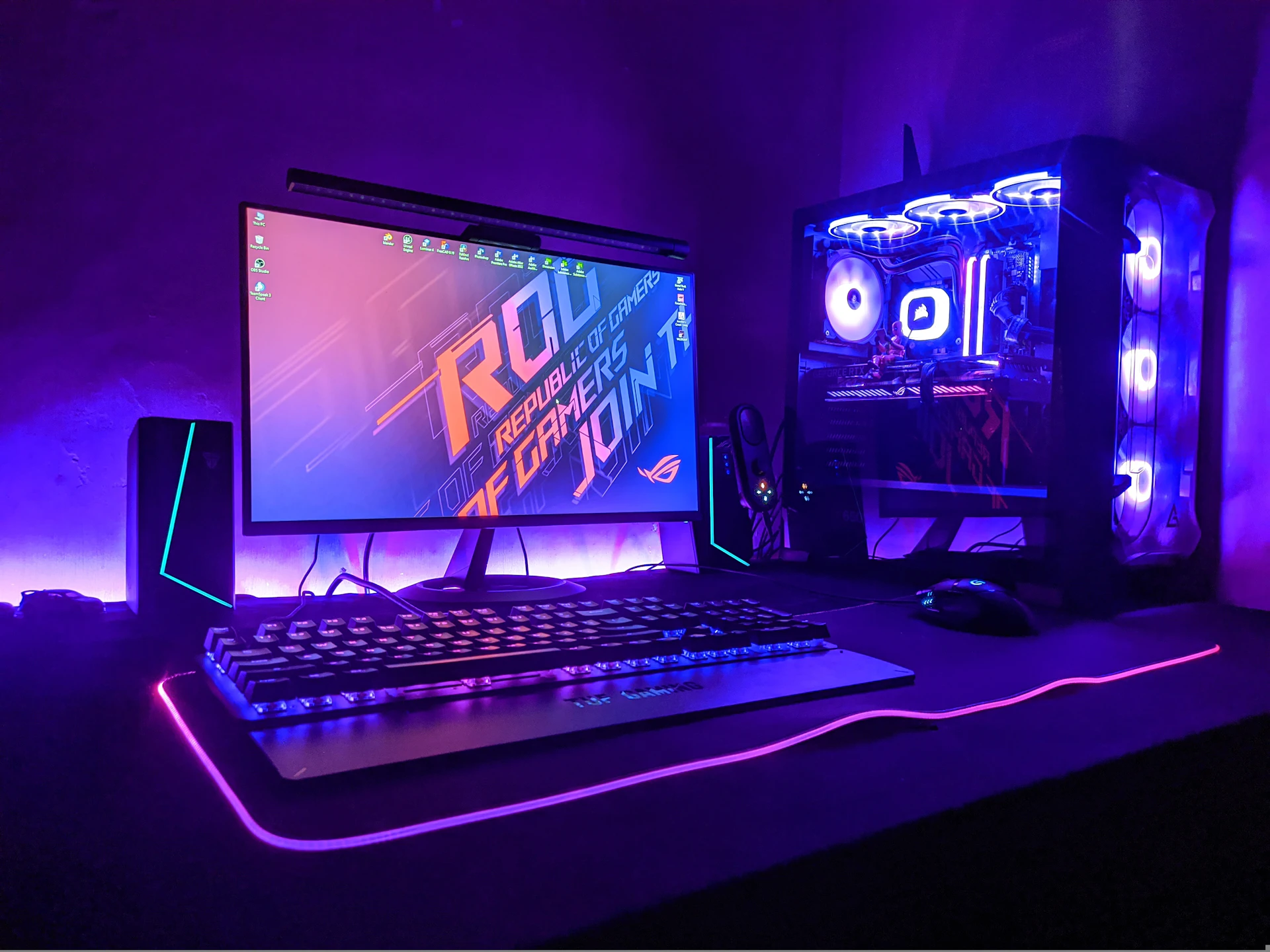 Een gaming-pc met glazen zijpaneel en blauwe verlichting naast een beeldscherm en toetsenbord