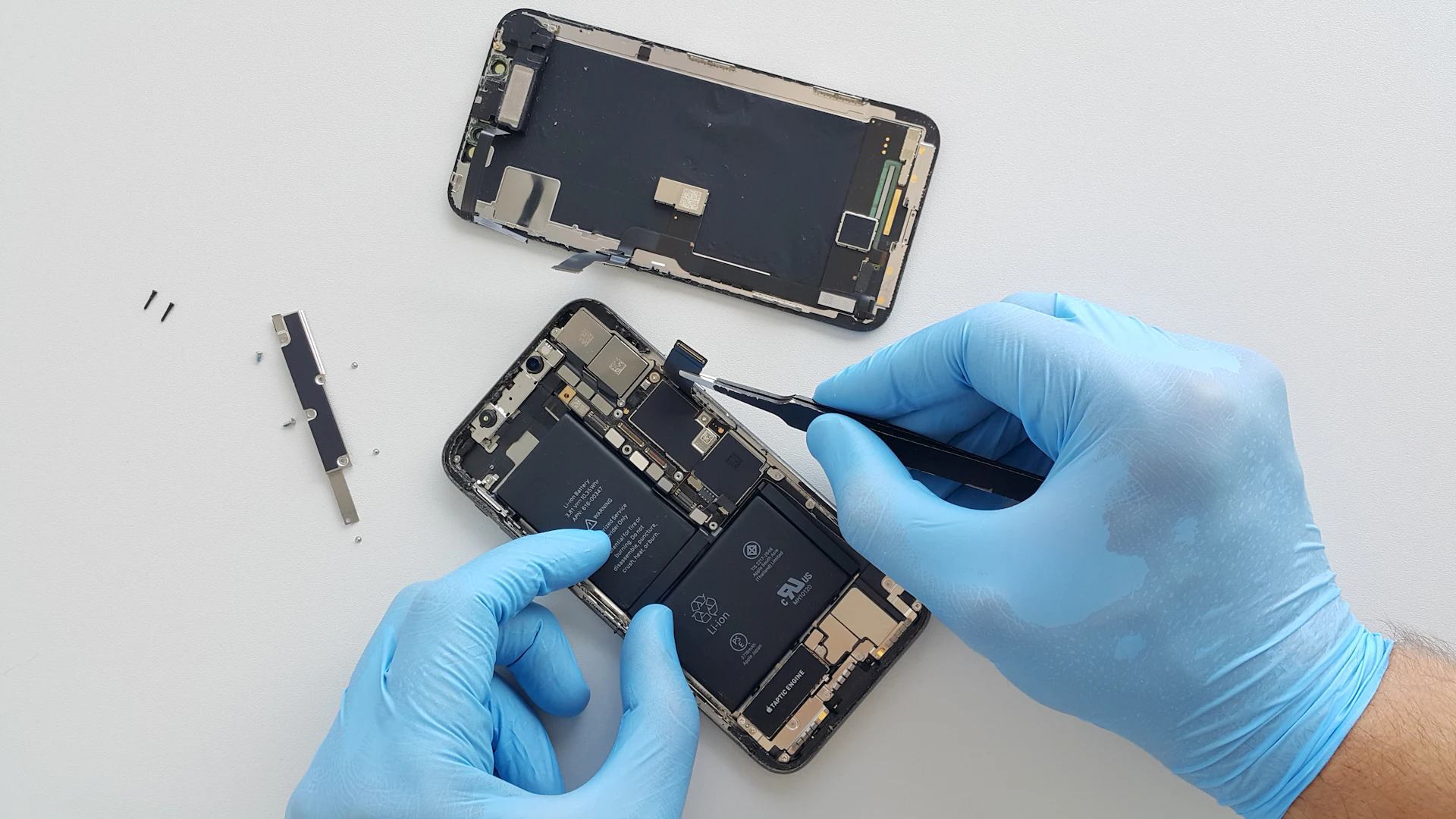 Een technicus met handschoenen repareert een geopende smartphone
